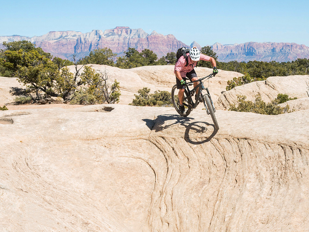 A certified IMBA Epic, the Gooseberry Mesa trail system is a must-do, classic ride. In this photo, Park City resident, Todd Winzenried, drops in on a slickrock halfpipe on Gooseberry's North Rim Trail, with the cliffs of Zion National Park in the background. Photo by John Shafer/Photo-John.net